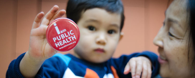 Toddler holding I am Public Health pin