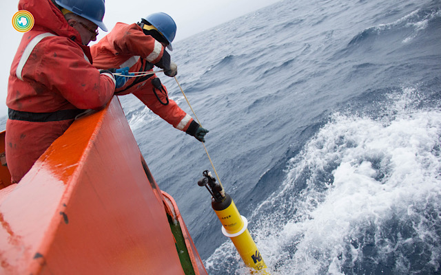 Two researchers deploy a robotic float into the ocean off a ship.
