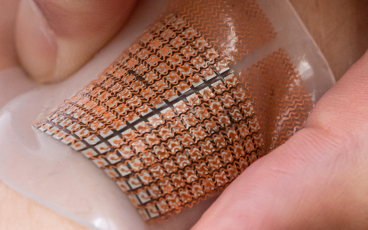 Two fingers press down on a soft, electronic patch against the skin.