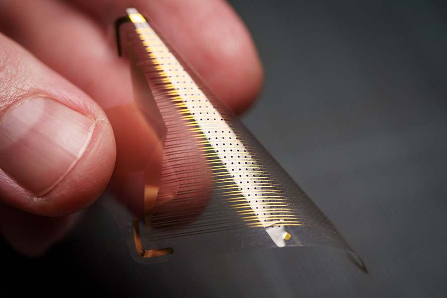 Thin, transparent, plastic-like square of electronic sensors being bent by a person's fingers.
